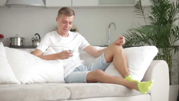 Мужчина сидит на диване с сотовым телефоном — стоковое видео