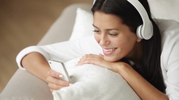 Girl in headphones on sofa using cellphone — Stock Video