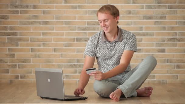 Парень, сидящий на полу с ноутбуком — стоковое видео