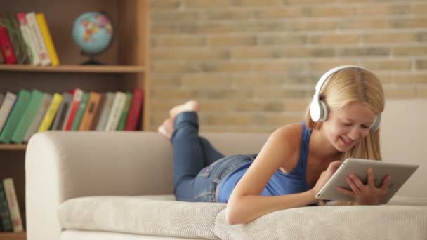 Κοπέλα φορώντας ακουστικά ξαπλωμένη στον καναπέ — Αρχείο Βίντεο