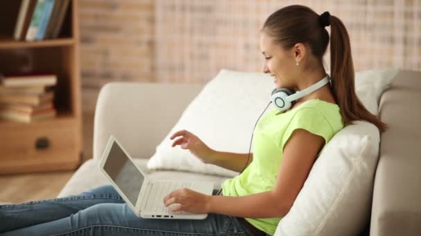 Chica en auriculares sentado en el sofá — Vídeos de Stock