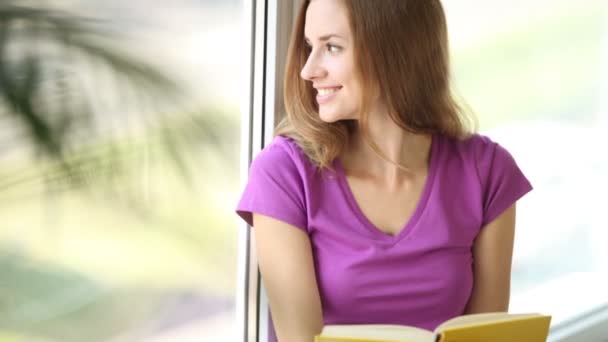 Chica sentada por la ventana leyendo — Vídeo de stock