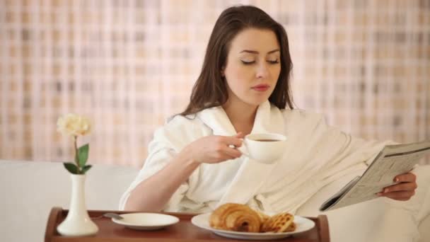 Linda chica sentada en la cama leyendo el periódico — Vídeos de Stock