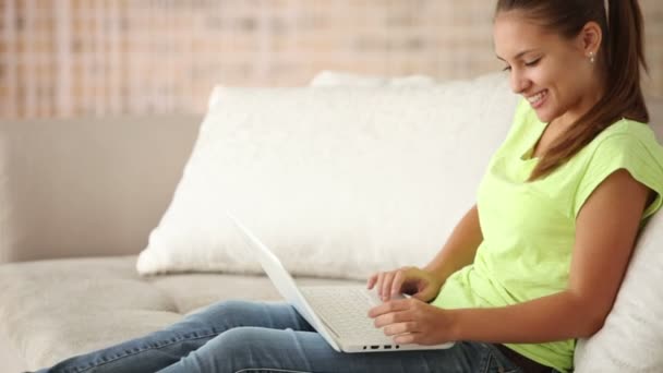 Glad flicka sitter på soffan med laptop — Stockvideo