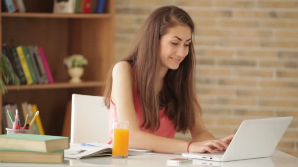 Chica sentada en el escritorio usando el ordenador portátil — Vídeos de Stock