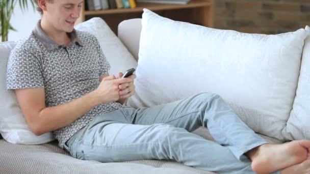 Τύπος χαλαρωτικό στον καναπέ που χρησιμοποιούν κινητό τηλέφωνο — Αρχείο Βίντεο