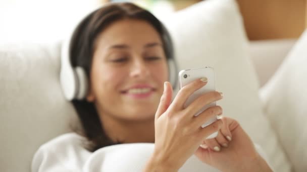 Дівчина в навушниках на дивані за допомогою мобільного телефону — стокове відео