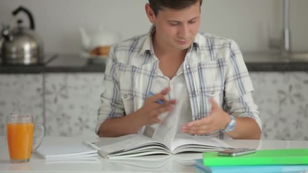 Хлопець вчиться за столом писати в блокноті і посміхається на камеру — стокове відео