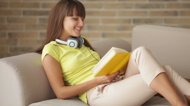 Chica sentada en sofá con libro — Vídeo de stock