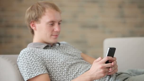 Хлопець розслабляється на дивані за допомогою мобільного телефону — стокове відео