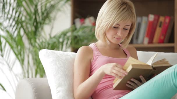 Chica sentada en sofá libro de lectura — Vídeos de Stock