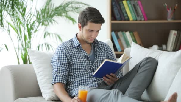 Молодий чоловік розслабляється на дивані читаючи — стокове відео