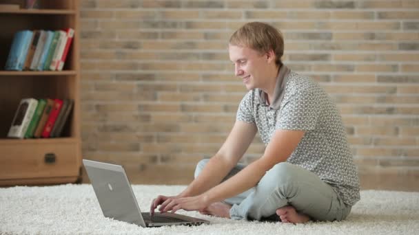 Хлопець сидить на підлозі за допомогою ноутбука — стокове відео