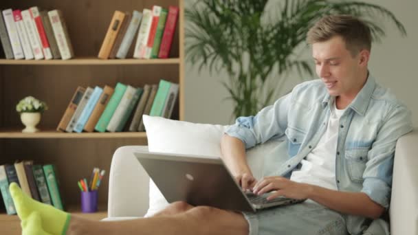 Student sitter på soffan och använder bärbar dator. — Stockvideo