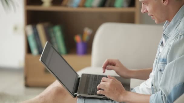 Чоловік сидить на дивані і використовує ноутбук — стокове відео