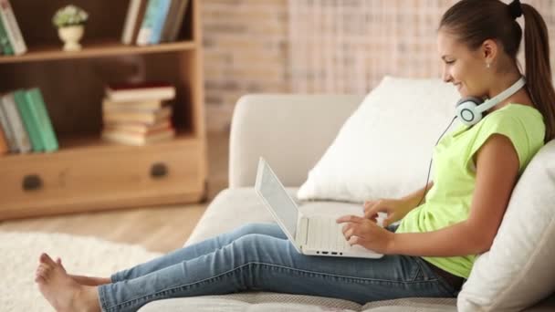 Девушка сидит на диване с ноутбуком — стоковое видео