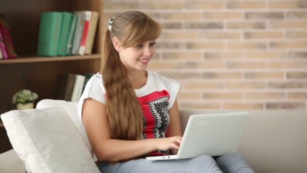 Chica sentada en el sofá utilizando el ordenador portátil — Vídeo de stock