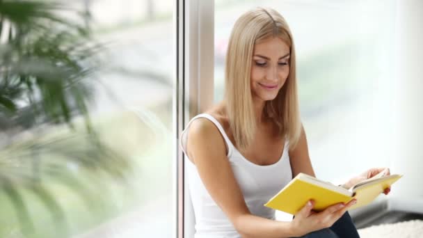 Dívka sedí u okna, čtení knihy — Stock video