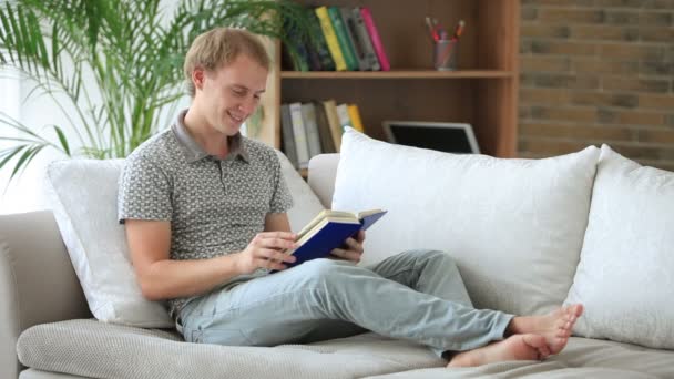 Mann sitzt auf Sofa und liest Buch — Stockvideo