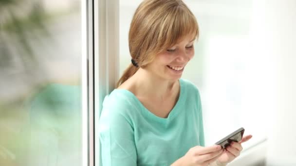 Mädchen sitzt mit Handy am Fenster — Stockvideo