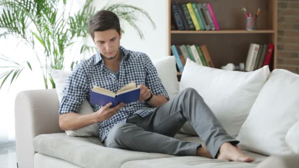 Homme assis sur le canapé avec livre — Video