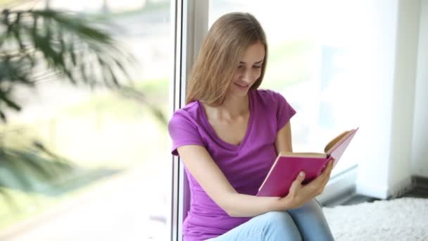 Dívka sedí u okna, čtení knihy — Stock video