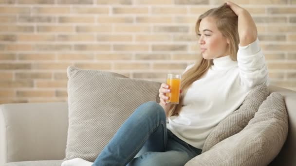 Милая девушка, сидящая на диване и пьющая сок — стоковое видео
