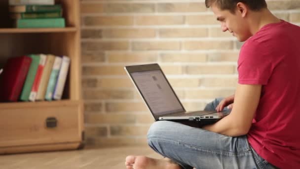 Чоловік сидить на підлозі за допомогою ноутбука — стокове відео
