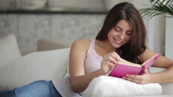 Beautiful girl sitting on couch reading — Stock Video