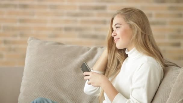 Κοπέλα καθόταν στον καναπέ, χρησιμοποιώντας το κινητό τηλέφωνο — Αρχείο Βίντεο