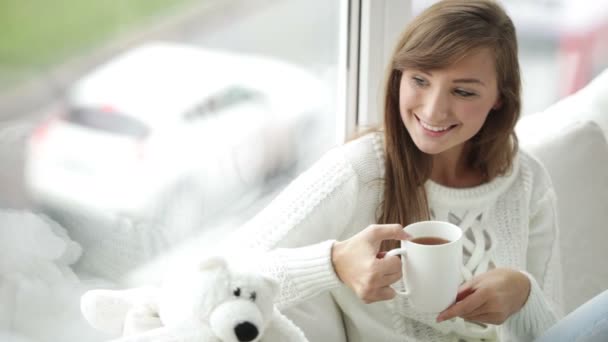 Girl sitting by window drinking tea — Stock Video