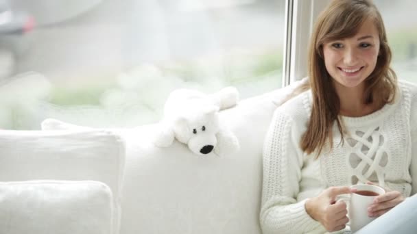 Chica feliz sentada junto a la ventana sosteniendo taza — Vídeos de Stock