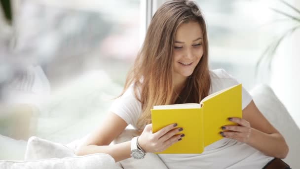 Chica sentado por ventana lectura libro — Vídeos de Stock