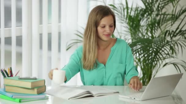 Flickan sitter vid skrivbord med böcker med laptop — Stockvideo
