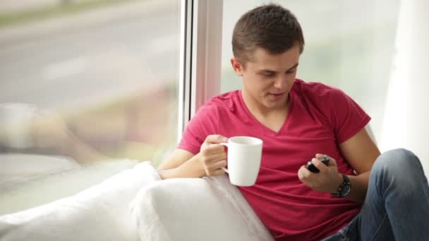Man met kopje thee met behulp van mobiele telefoon — Stockvideo