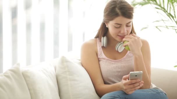 Dívka, která nosí sluchátka sedět na pohovce — Stock video