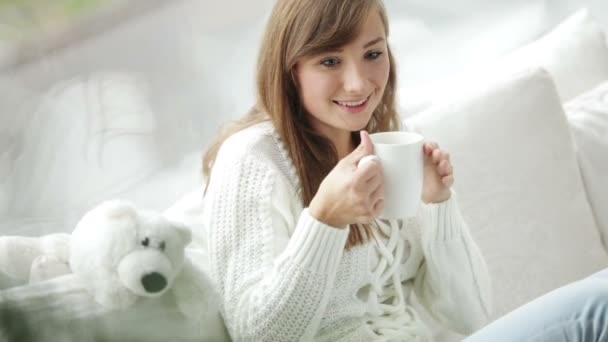 Девушка сидит у окна и пьет чай — стоковое видео