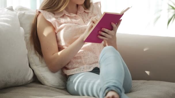 Дівчина сидить на дивані читає книгу — стокове відео