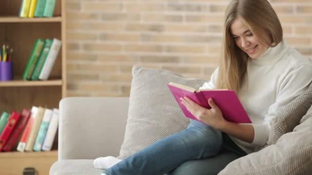 Девочка, сидящая на диване и читающая книгу — стоковое видео