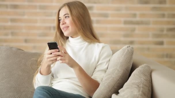 Flicka sitter på soffan med mobiltelefon — Stockvideo