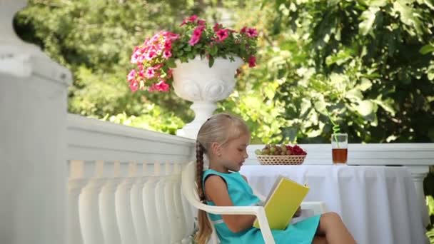 Preschooler κορίτσι διαβάζοντας ένα βιβλίο στον κήπο. Παιδί χωροθέτηση σε μια καρέκλα στο τραπέζι. — Αρχείο Βίντεο
