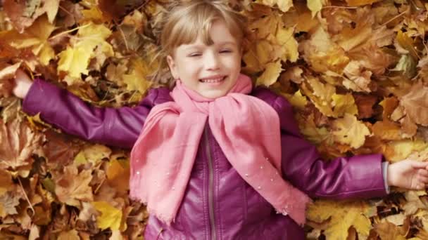 Маленькая девочка лежит в желтых листьях . — стоковое видео