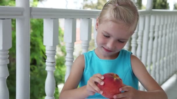 Petite fille avec une grosse pêche rouge . — Video