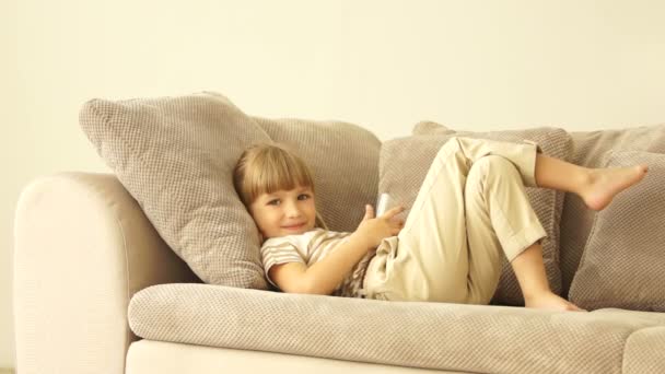 Маленька дівчинка лежить на дивані з телефоном — стокове відео