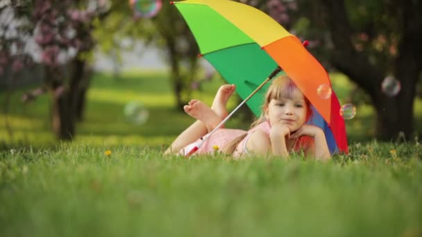 Маленькая девочка лежит на траве с омреллом — стоковое видео