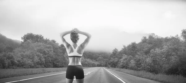 Mujer trotadora mirando por el tramo vacío de la carretera — Foto de Stock