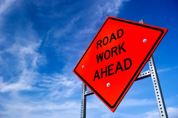Bright orange road work ahead sign against a blue sky with light clouds — Stock Photo, Image