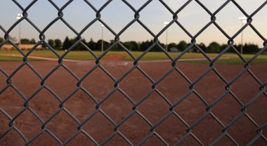A wide angle shot of a baseball field shot through a chain-link fence at dusk clipart