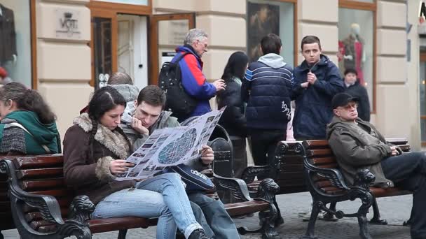 LVIV, UKRAINE - 28 février 2015 Deux touristes, hommes et femmes, étudiant une carte touristique assis sur un banc et entouré par une vie urbaine animée — Video