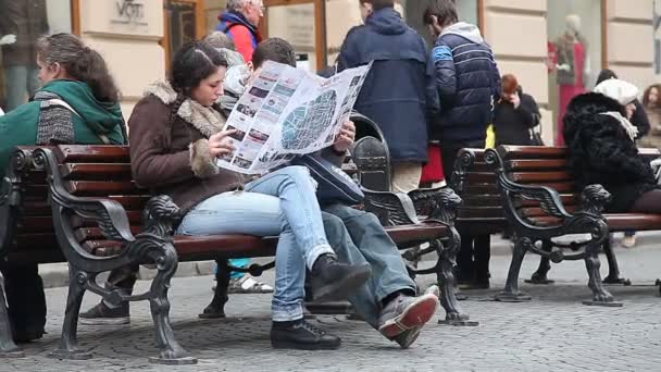 Lwów, Ukraina - 28 lutego 2015 dwóch turystów, mężczyzna i kobieta, studiując mapę zwiedzanie siedząc na ławce i jest otoczony przez męczącej codzienności — Wideo stockowe